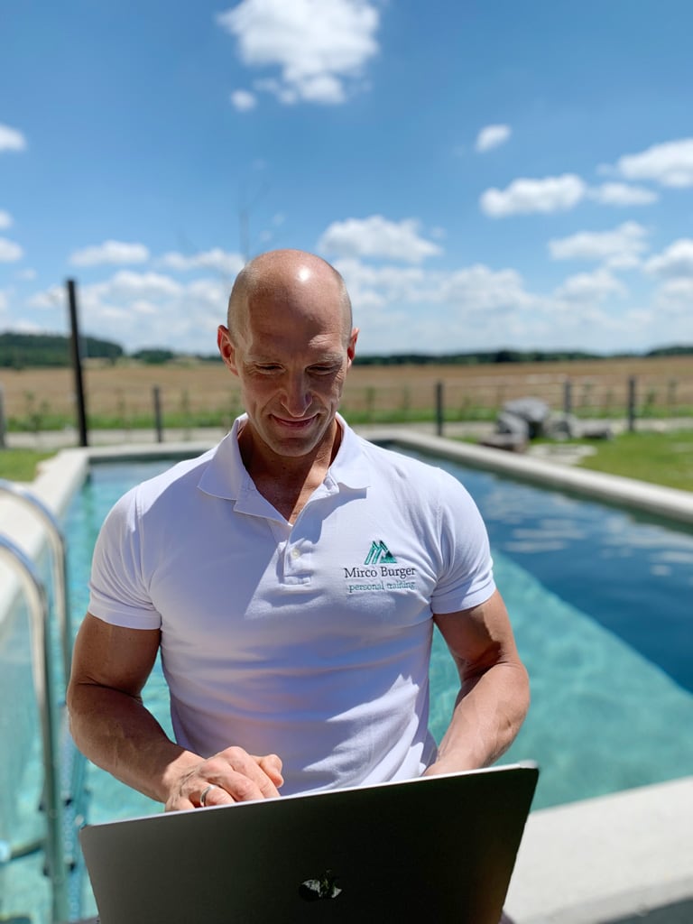 Der Coach sitzt am Laptop am Pool.